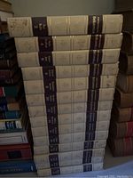 Stack of white Encyclopaedia Britannica books with dark blue and gold spine bands, volumes 2 through 16 visible.