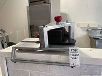 Full view of the commercial tomato slicer with multiple blades and red knob on top, placed on a counter.