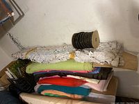 Stack of fabric bolts in various colors including white lace, green knit, red, orange, blue, brown, and pink