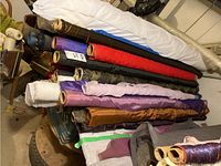 Photo showing bolts of fabric in various colors including white, black, red, purple, brown, camo pattern, and pink.