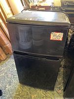 Front view of closed black Clairtone mini refrigerator model CLF31101B with sticker label, showing overall external condition.