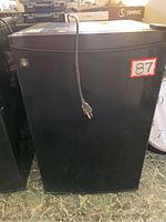 Front view of the black GE mini fridge showing single door and power cord.