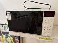 Full view of white Danby microwave oven with black glass door and power cord wrapped on top.