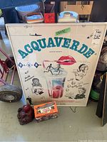 Framed Acquaverde print with turquoise text and vintage advertisement style art, showing a couple running into a beverage glass with straw, lips graphic, and multiple retro illustrations