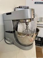 Side view of Kenwood stand mixer with stainless steel bowl and whisk attachment fitted, user instructions inside bowl.