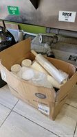 Box with stacks of white disposable coffee cups, clear plastic cups, white soup cups, some coffee cup lids, and a roll of cling wrap inside a cardboard box.