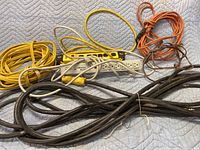 Photo showing 4 extension cords of different lengths and thicknesses, and 2 surge protectors on a padded surface.