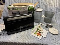 Overview of FoodSaver 3400 Series vacuum sealer, original box, two transparent canisters (one with lid, one missing lid), multiple hoses, vacuum bags, and mason jar lid.