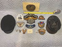 Overview photo showing collection of patches, pins, two caps, and carved sculpture alongside a tape measure for scale.