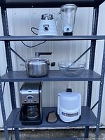 Shelf display of five kitchen appliances: juicer and blender on top shelf, pressure cooker and glass bowl on middle shelf, coffee maker and juicer base on bottom shelf.
