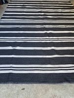 Full view of large rectangular rug showing black base color with white horizontal stripes and some creasing or wrinkling.