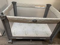 Graco Pack N Play collapsible crib/playpen/bassinet with mesh sides and mattress inside.