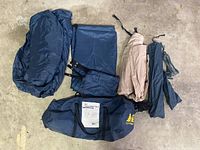 Blue and beige tent fabric and components laid out on a concrete floor alongside a dark blue carrying bag with REI branding.