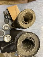 Two partially used rolls of black roofing felt material; rolls appear approximately 40 and 36 units long, about 1.25 inches thick at the top of the roll; visible surrounding tape and sealant supplies.