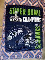 Full view of the folded navy fleece blanket with large green and white text and Seahawks helmet graphic.