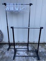 Two adjustable metal clothes racks shown side by side with one holding white plastic hangers.