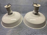 Pair of white dome-shaped industrial light fixtures shown from the side on a padded surface.
