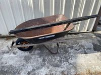 Side view of rusty metal wheelbarrow with attached wooden handles and one black new wheel.