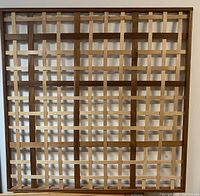 Full view of woven wooden square artwork mounted on wall showing grid pattern of light and dark wood strips.