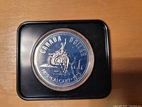 Reverse side of the 1975 Calgary Centennial Silver Dollar depicting a rider on horseback with the Calgary Tower in the background, in a protective holder.