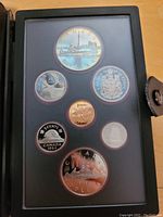 Photo of full 1984 Canadian coin set including the large commemorative double dollar and six additional coins in protective folder.