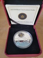 Photo of the silver commemorative coin inside a protective case with Certificate of Authenticity in the background.