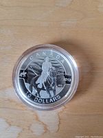 Reverse side of silver coin depicting Royal Canadian Mounted Police officer on horseback with dog and maple leaf background, and coin details.
