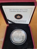 Silver coin in protective casing inside red velvet lined case, with certificate of authenticity visible.