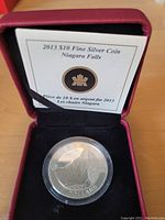 Overall view of 2013 Canadian $10 fine silver coin in protective clear capsule and red presentation case with COA behind.