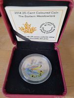 Photo of the 2014 25 cent coloured coin featuring the Eastern Meadowlark bird inside a protective capsule and black display case with certificate on upper lid.