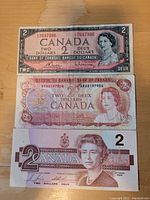 Front view of the three Canadian 2 dollar bills stacked showing dated designs from 1954, 1974, and 1986.