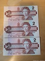 Front side of three Canadian $2 bills featuring Queen Elizabeth II portrait.