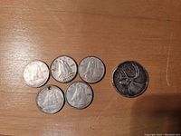 Five Canadian dimes dated 1943 and one Canadian quarter with a caribou design on a wooden surface.