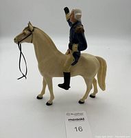 Side view of George Washington figurine dressed in blue riding a beige horse with bridle; missing hat, sword, and flag.