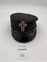 Front view of black Knights Templar Masonic hat showing red cross emblem on front and black leather visor with slight wear.