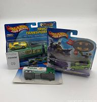 Photo of all 3 unopened Hot Wheels die-cast trucks including the yellow-green Truckin Transporters set, Batmobile vs. the Riddler truck, and the Tropicana Hauler.