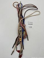 Group photo showing 8 bolo ties with cords in tan, brown, blue, pink, and metal tips, some with decorative stones and ornaments