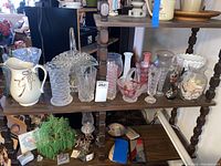 Multiple vases including milk glass, crystal, and ceramic pitcher arranged on wooden shelving unit.