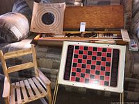 Full view of all items showing the archery set in wooden case open with arrows and bow, paper target on back, foldable checkers board and child's rocker chair