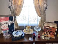 Overview of lot showing all items on table beneath window with lace curtains and gold drapes