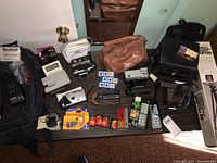 Photo showing multiple vintage cameras, accessories, films, flashbulbs, and camera cases on a table.