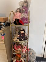 Shelf showing three china dolls and various stuffed animals placed on a metal rack.