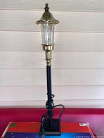 Decorative metal street lamp with glass/plastic globe and electric cord on red surface