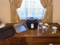 Photo showing 4 pedestal mugs, 3 large cooking pots, and 2 baking pans arranged on wooden surface near window