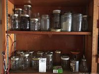 Shelf displaying various sizes of clear glass mason jars, some with metal lids and rings, glass coffee carafes, and a glass cookie jar.