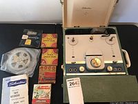 Full view of Silvertone reel to reel tape recorder with magnetic tape and multiple 16mm film boxes displayed alongside the open unit inside its green case.