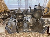 Full view of vintage pewter tea set on tray including teapot, coffee pot, creamer, sugar bowl, and showing tassel-handled fork and token on the tray