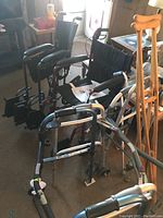 Overall view showing 2 collapsible wheelchairs, 2 foldable walkers, wooden crutches, and canes grouped together