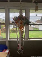 Macrame plant hanger holding artificial orange and pink flowers, hanging indoors by window