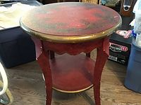 Round red and gold trim Art Deco side table, showing top, legs and lower shelf with scalloped apron detail.